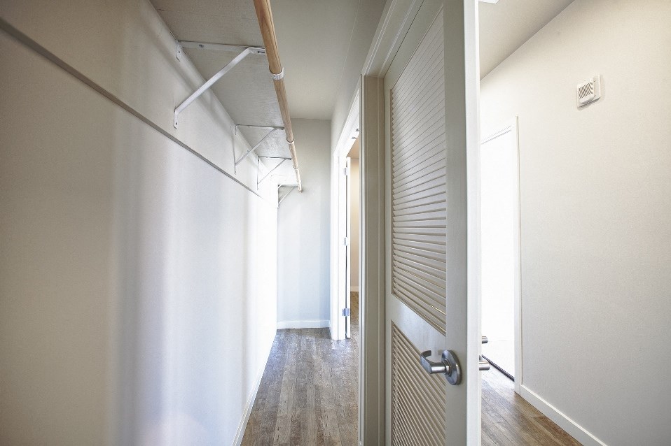 a hallway with white walls and wood floors and a closet with white doors