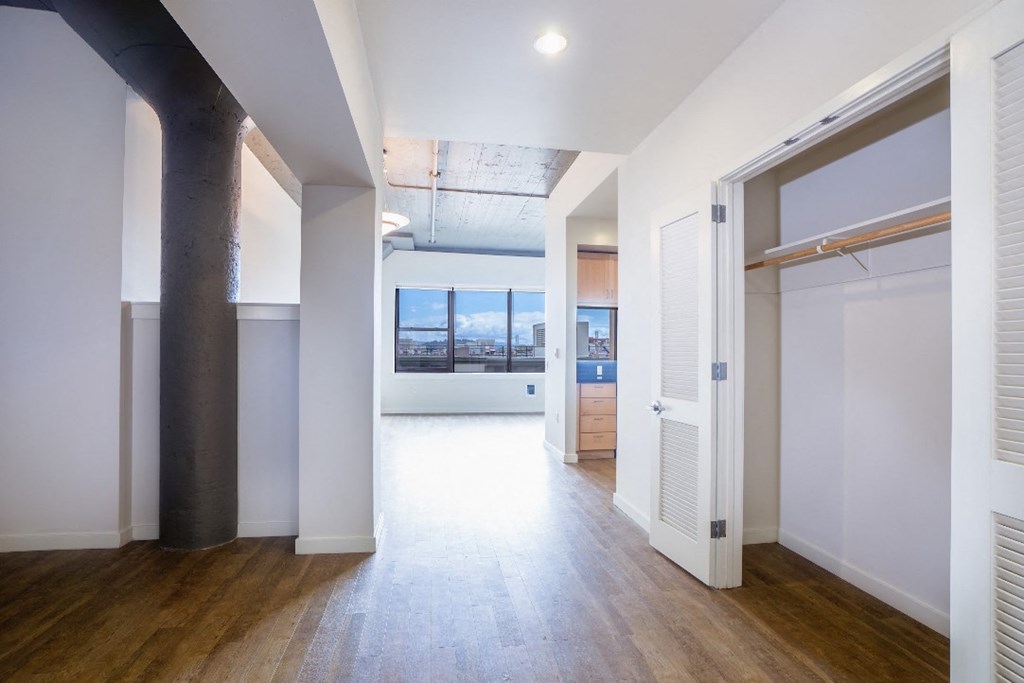 a living room with white walls and a wooden floor and a door to a kitchen