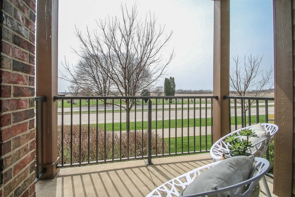 a balcony with chairs and a view of a field and a tree