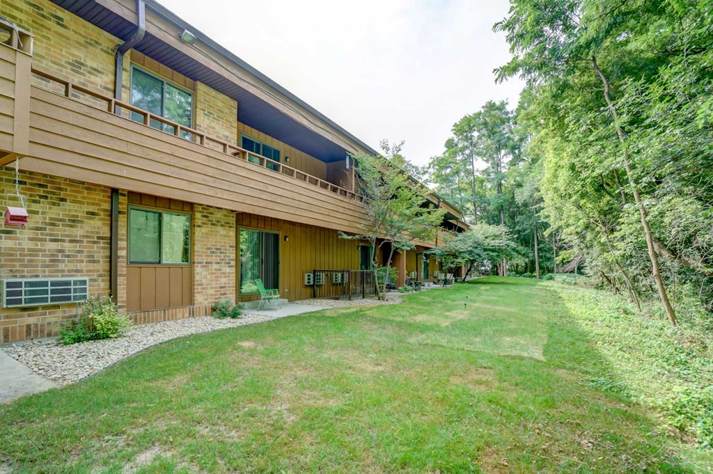 the side of a house with a green lawn and trees