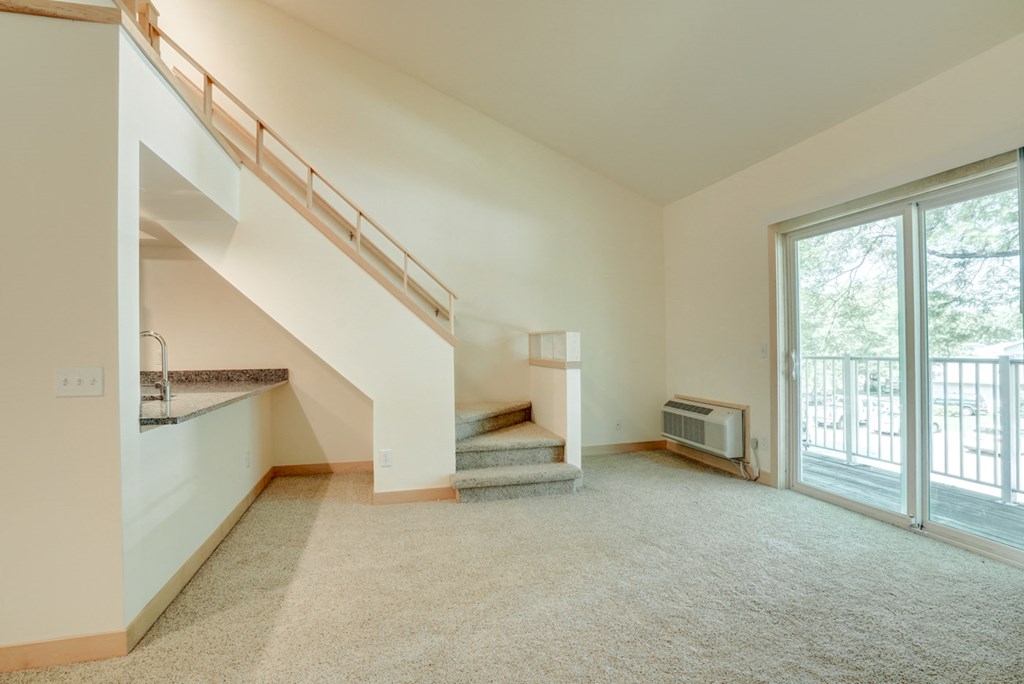 an empty living room with a staircase and a door to a balcony