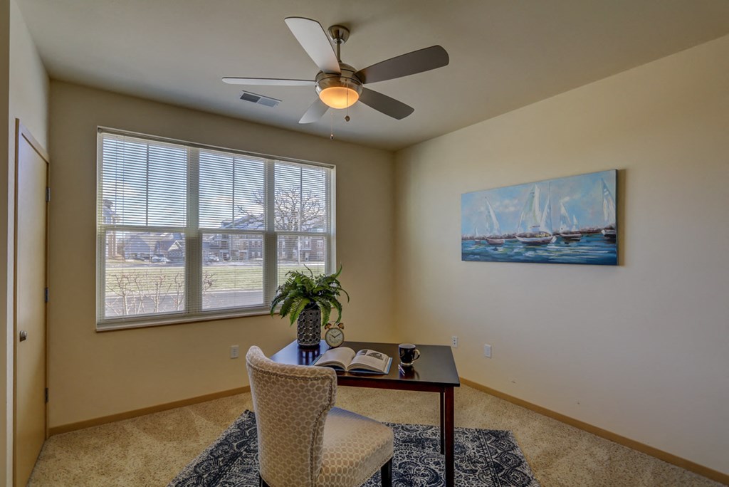 a living room with a desk and a ceiling fan