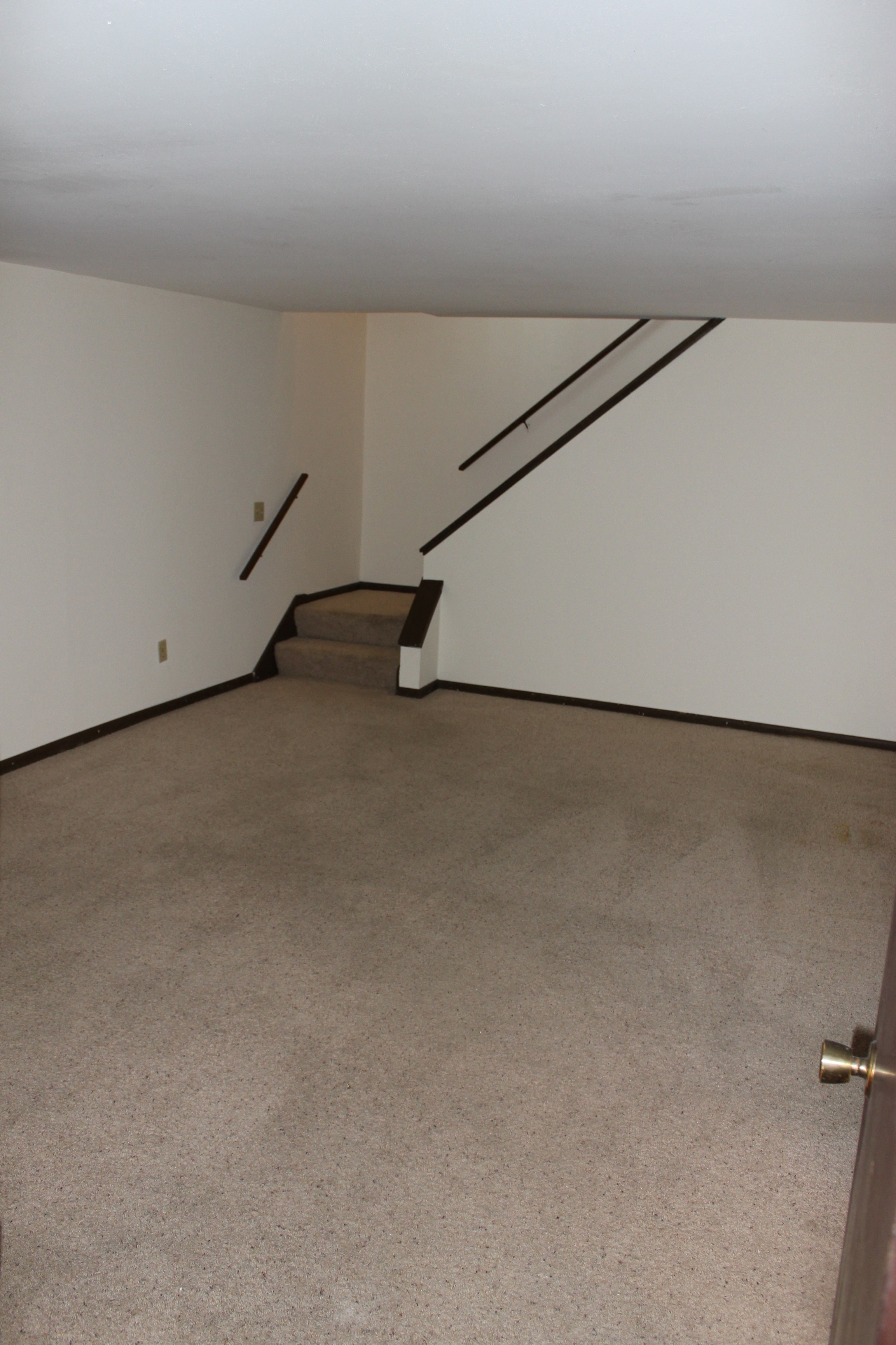 a living room with white walls and a staircase in the corner
