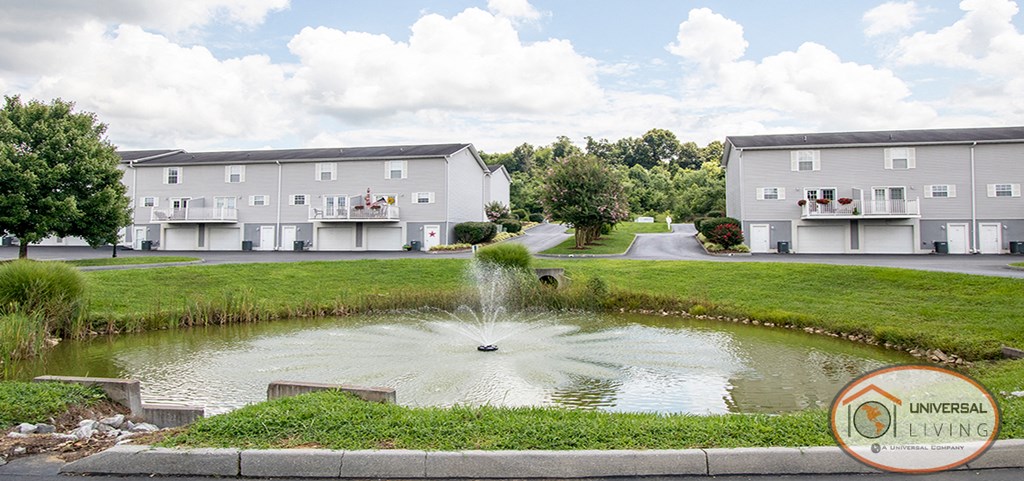 a fountain in the middle of a pond in front of apartment buildings