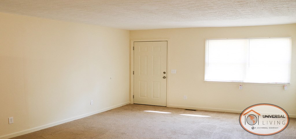 an empty living room with a white door and a window