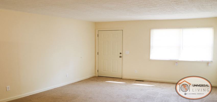 an empty living room with a white door and a window