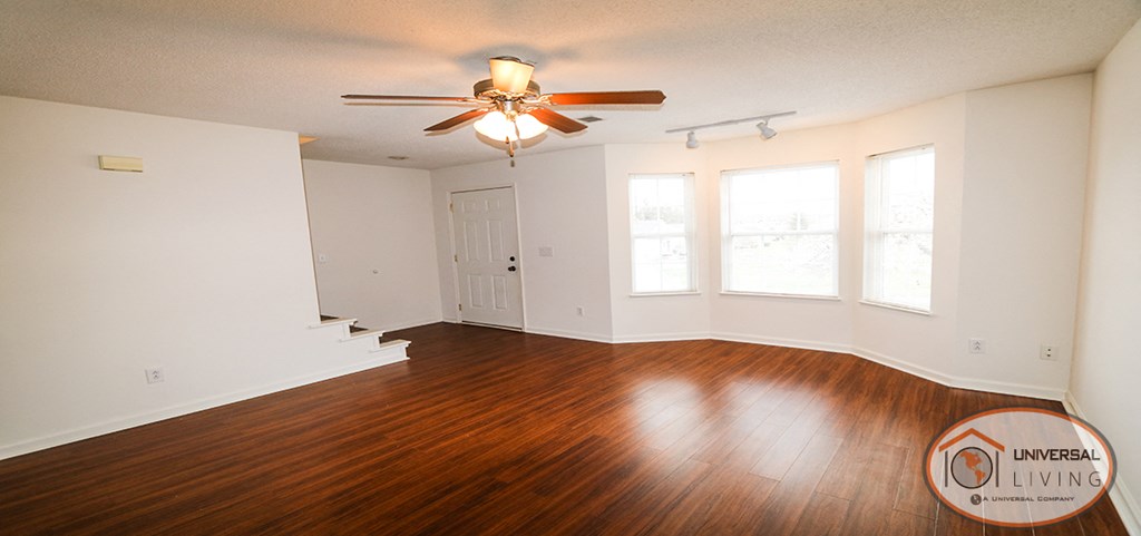 an empty living room with wood floors and a ceiling fan