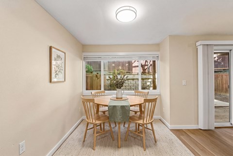Dining area with a round table and four chairs, a window, and a sliding door with vertical blinds to a patio.