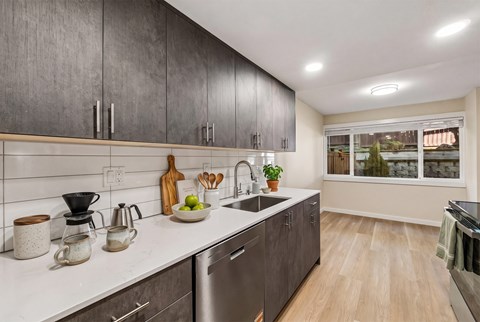 Galley kitchen with dark wood-tone cabinets, white stone-look counters, subway tile, and a stainless dishwasher.