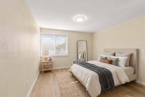 Bedroom with an upholstered queen bed, a leaning floor mirror, a nightstand, and a window with blinds.