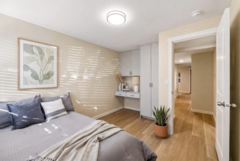 Bedroom with a built-in desk, overhead cabinets, a tall wardrobe, and a doorway opening to the hallway.