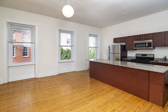 an empty living room with a kitchen with wood floors