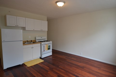 an empty kitchen with white appliances and a wooden floor