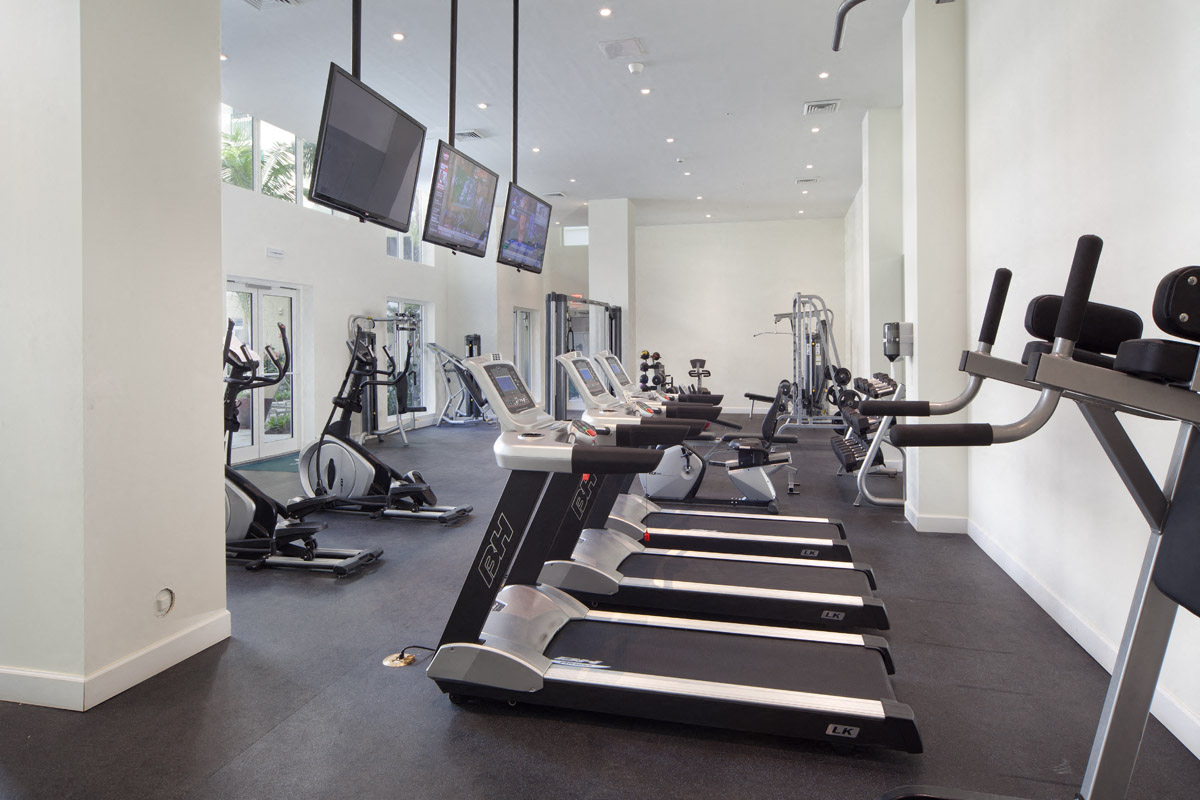 a gym filled with cardio equipment and flat screen televisions