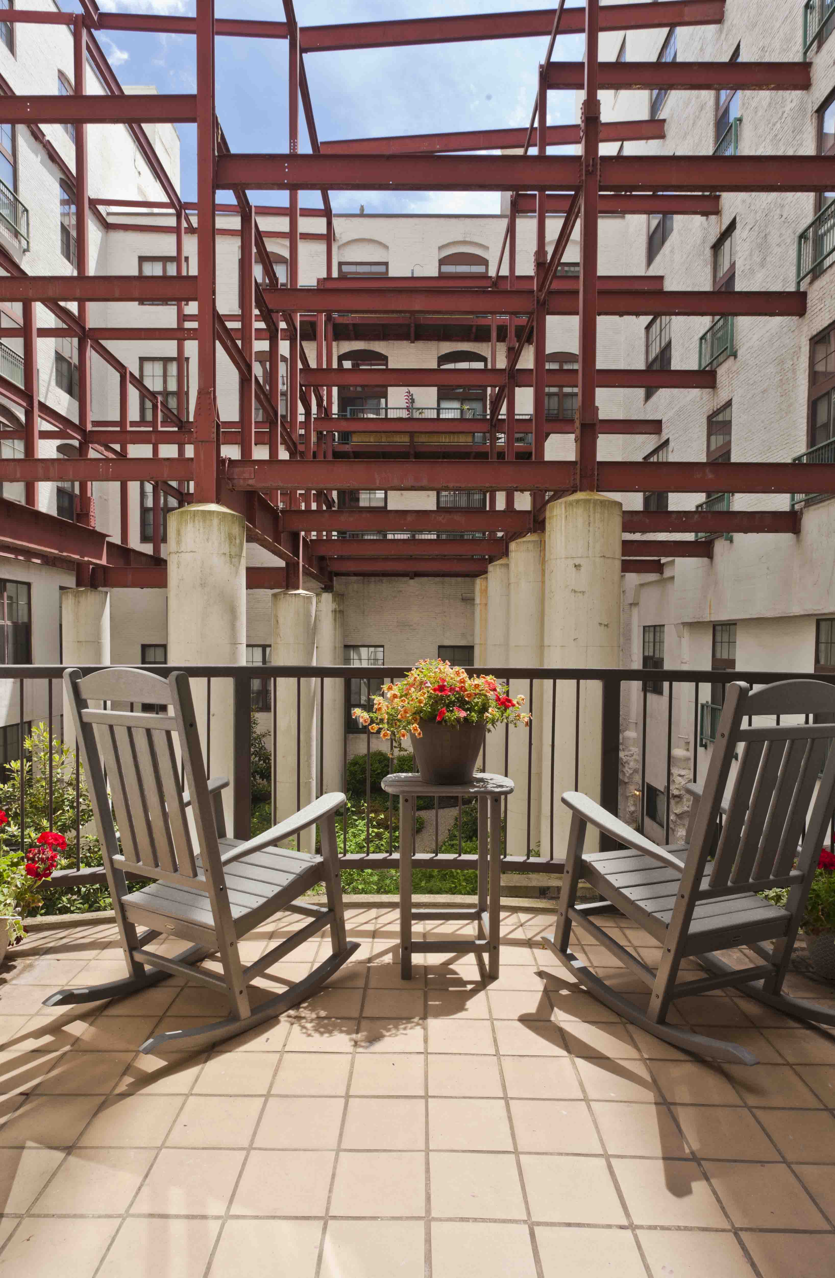 two wooden rocking chairs on a balcony with a table with flowers