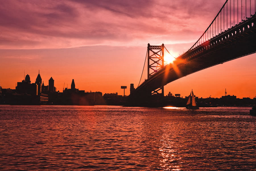 a sailboat passes under the bridge at sunset