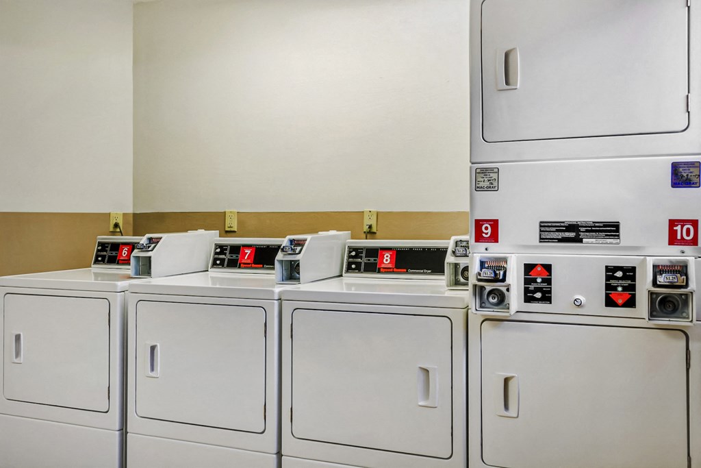 a row of washers and dryers in a laundry room with white cabinets