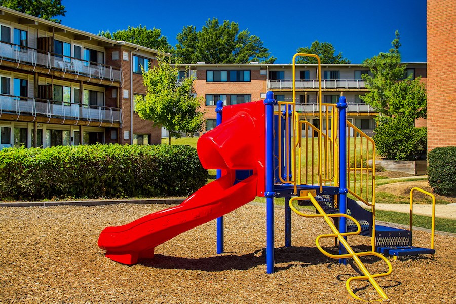 a playground with a red slide in front of an apartment building