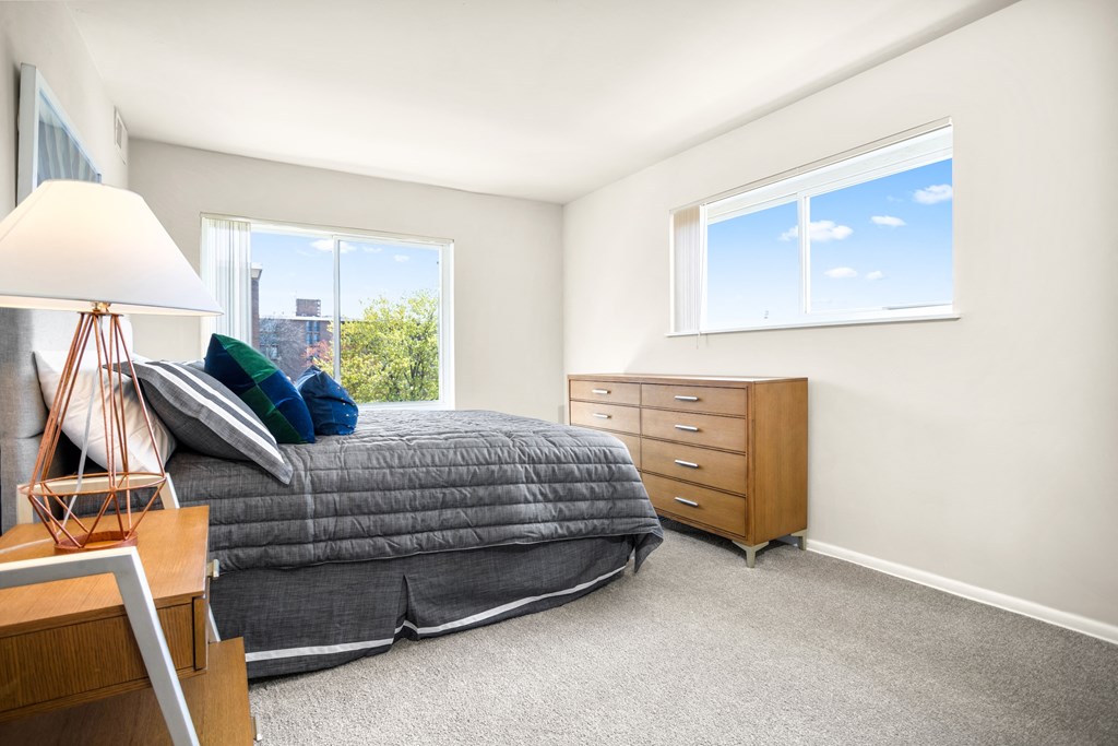 a bedroom with a bed and a dresser and two windows