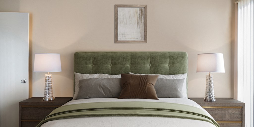 a bedroom with a bed with a green headboard and two lamps