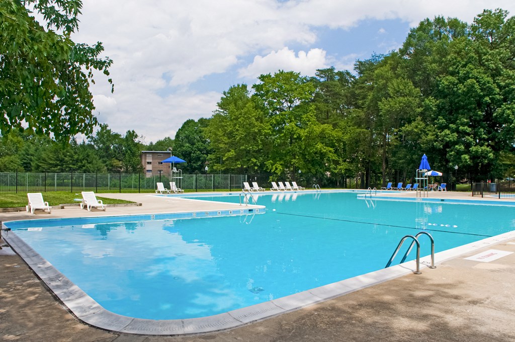 a swimming pool with chairs and trees in the background