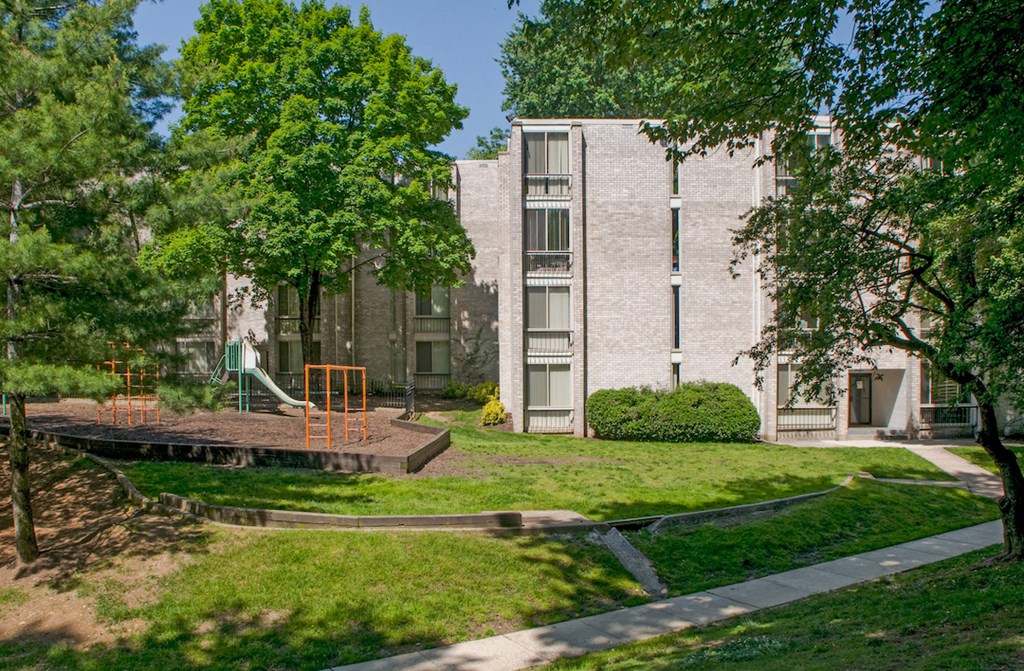 an apartment building with a yard and trees in front of it