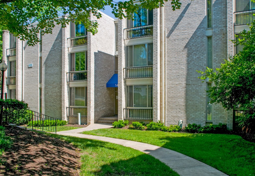 a walkway in front of a brick building with grass and trees