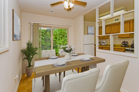A dining room with a table set for two and a potted plant on the side table.