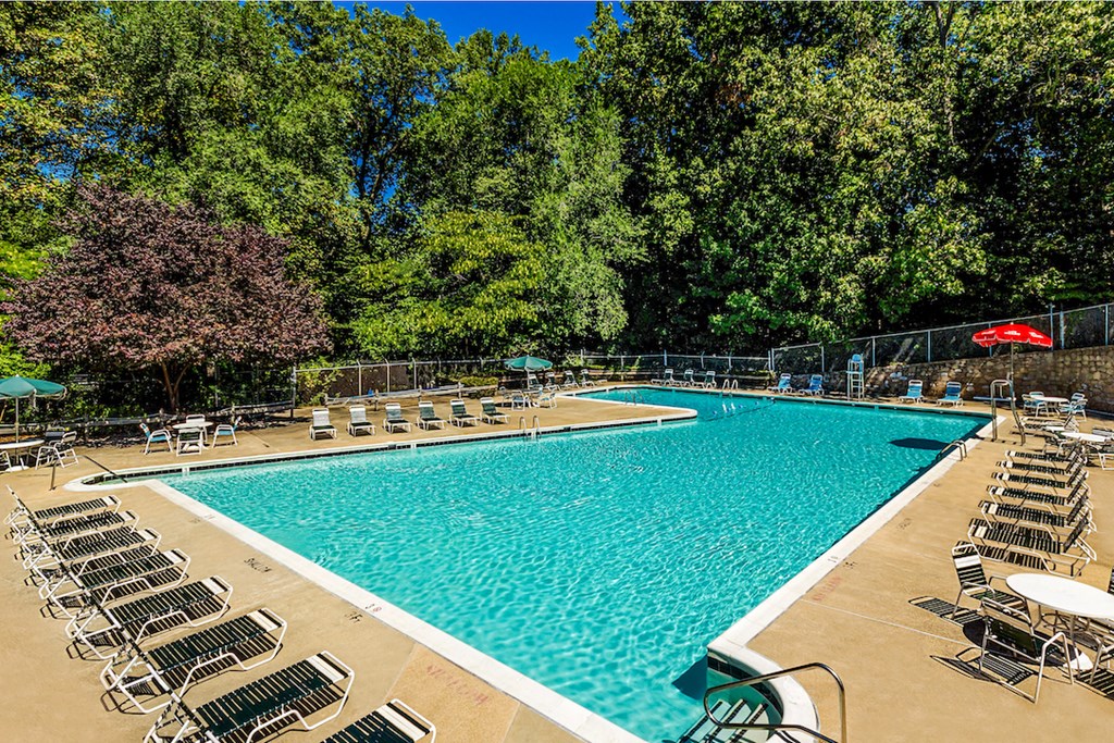 a swimming pool with chairs and trees in the background