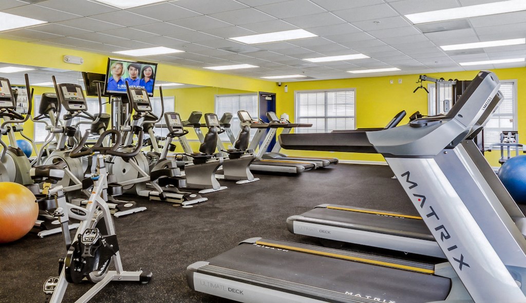 a gym with cardio equipment and weights in a building with yellow walls