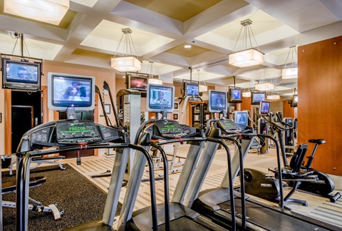 a gym with various cardio machines and televisions