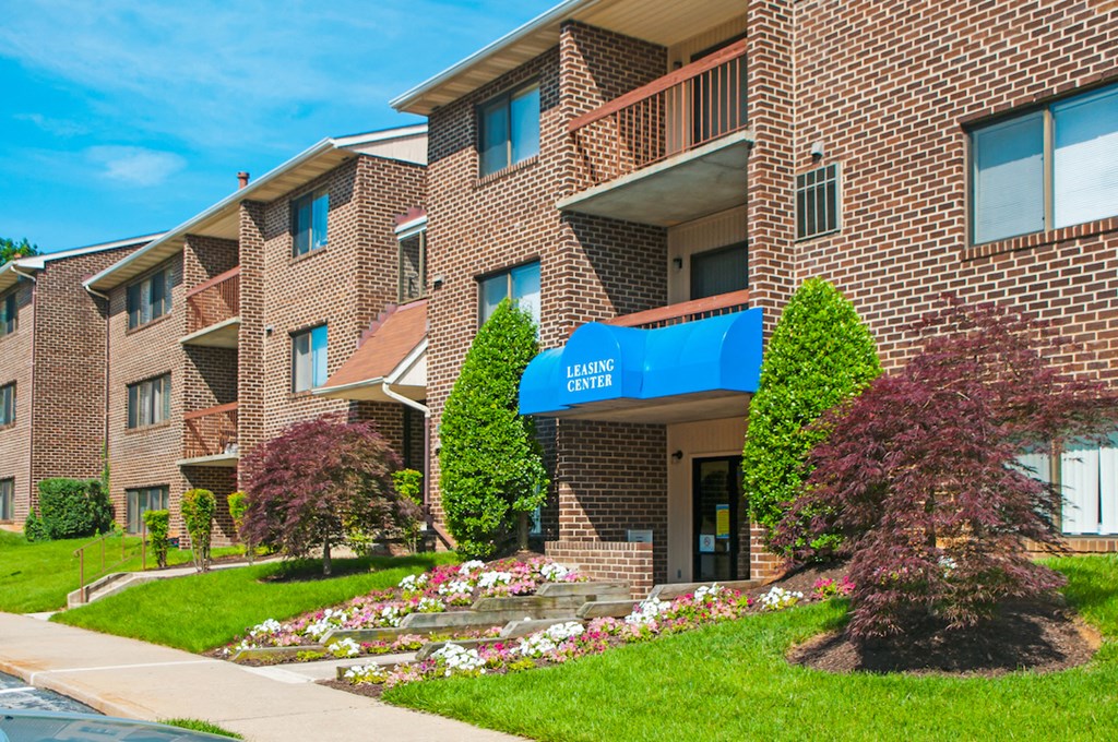 a brick apartment building with a blue awning and flower gardens