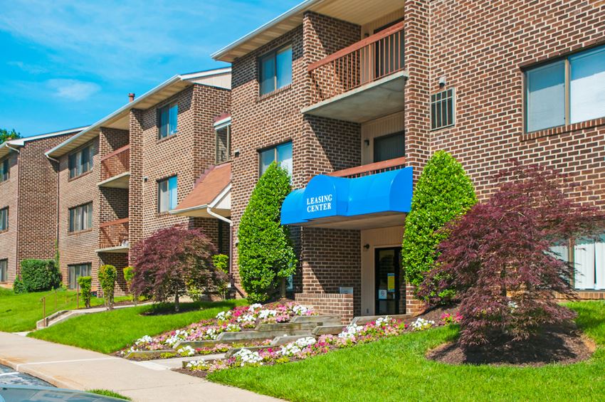 a brick apartment building with a blue awning and flower gardens