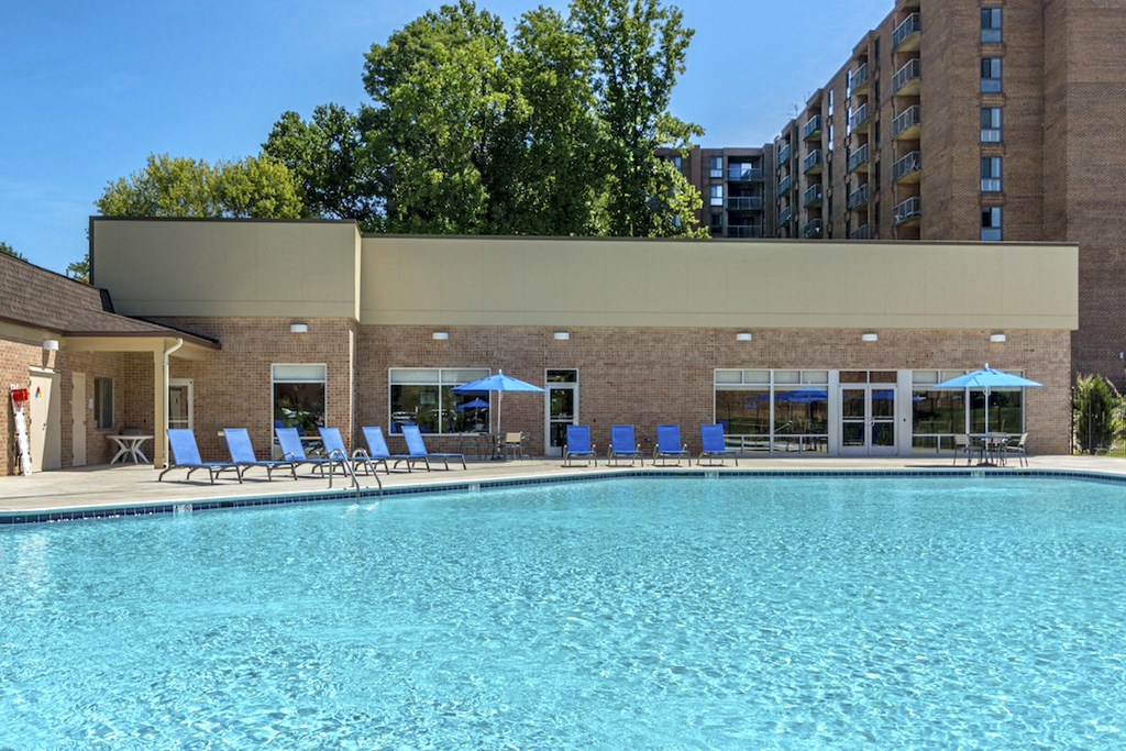 a swimming pool with blue chairs and a building in the background