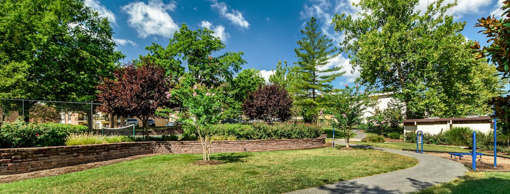 a pathway through a park with trees and a retaining wall