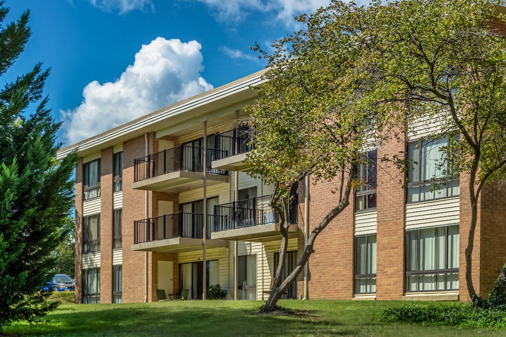 a brick apartment building with balconies and a tree in the yard