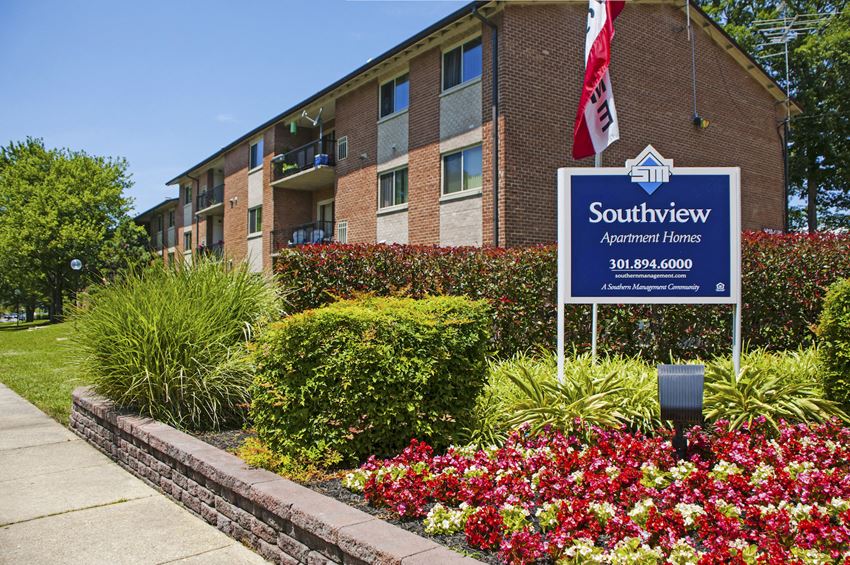 an apartment building with a sign in front of a flower garden