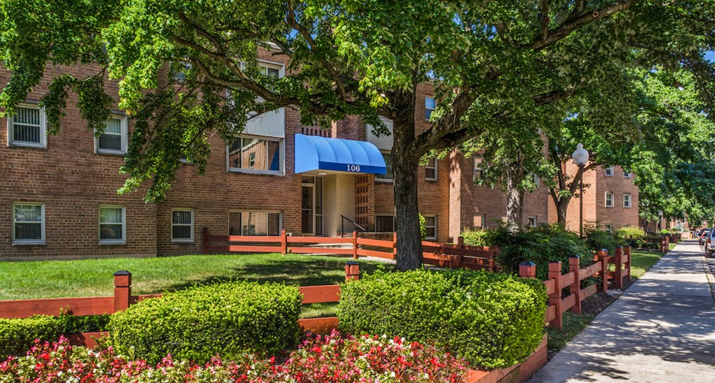 a sidewalk in front of a brick building with a tree and flowers