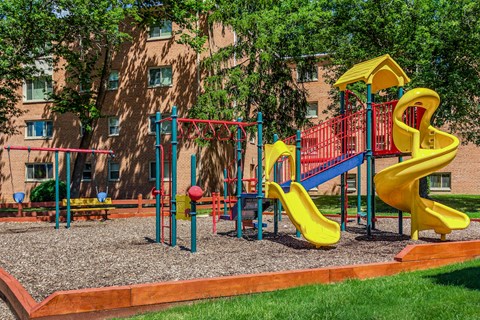 a playground with yellow and red toys in front of a building