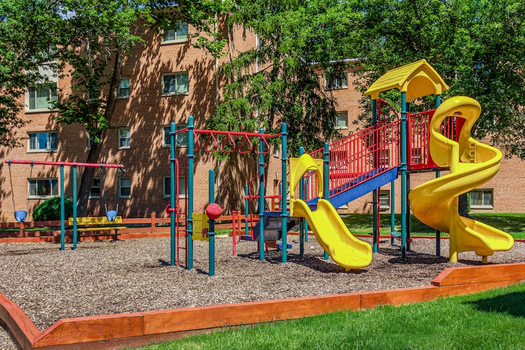 a playground with yellow and red toys in front of a building