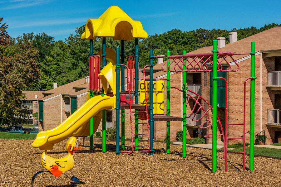 a childrens playground with a yellow slide and other playground equipment in front of apartments