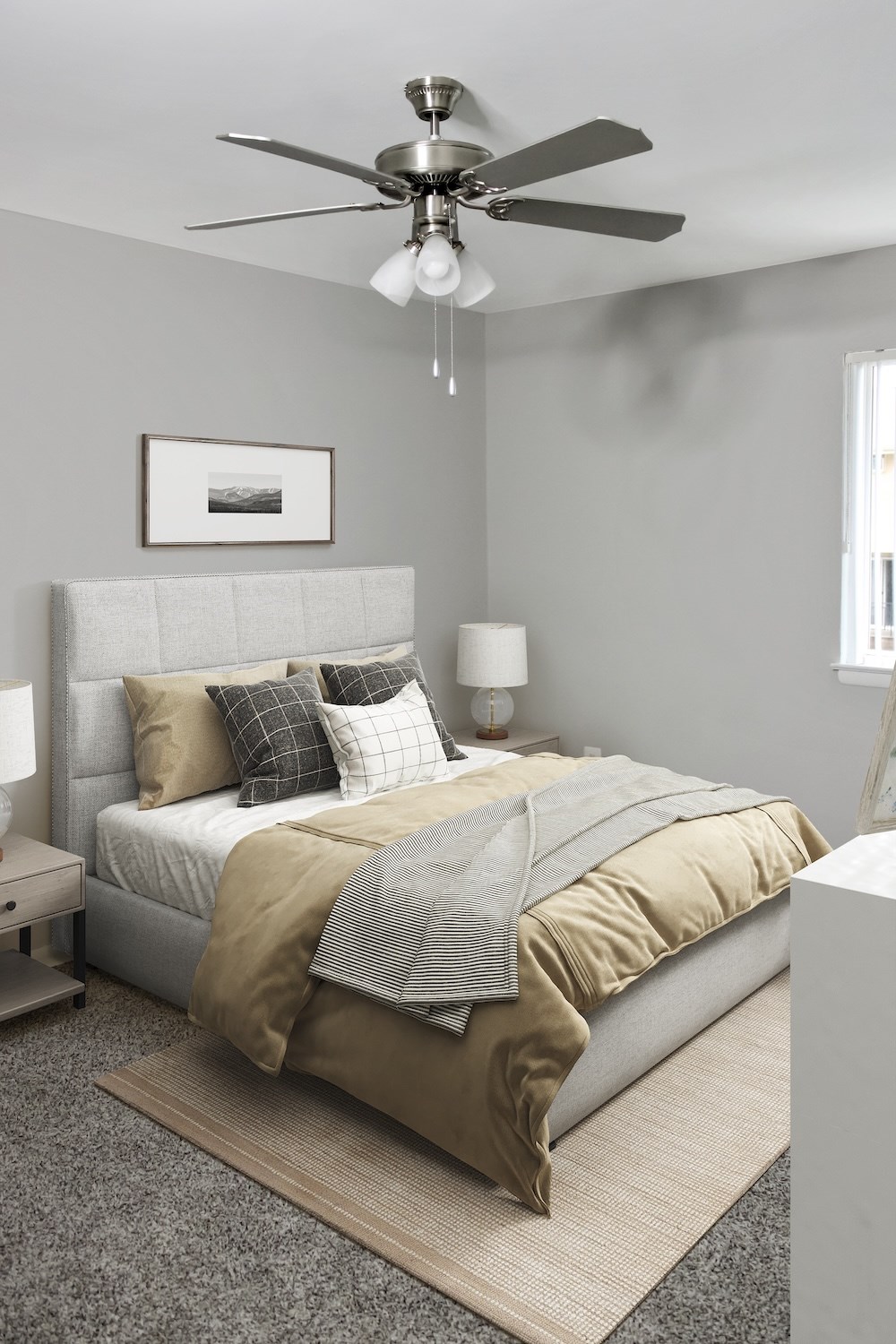 A bedroom with a bed, pillows, a blanket, a ceiling fan, and a picture on the wall.