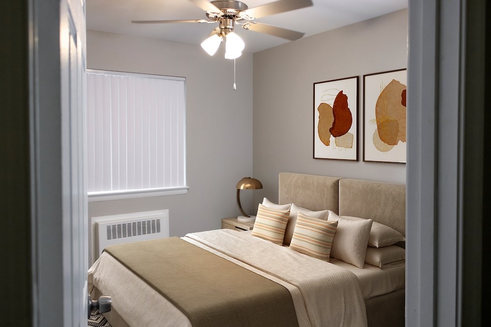 A bedroom with a bed, pillows, a ceiling fan, and two wall art pieces.