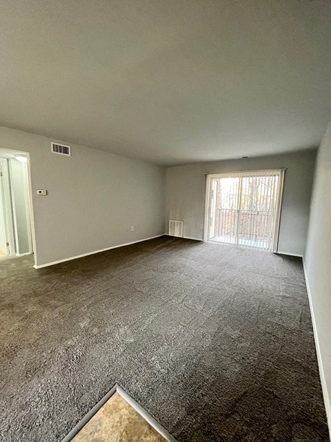 an empty living room with carpet and a sliding glass door