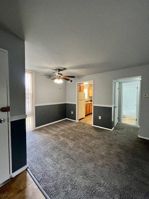 an empty living room with a ceiling fan and a door to a kitchen