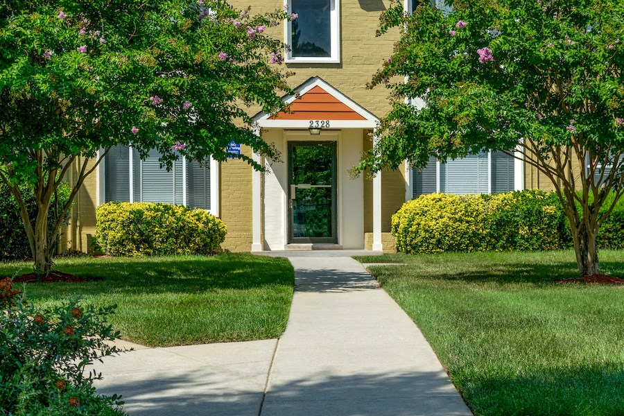 a sidewalk in front of a yellow house with a green lawn and trees