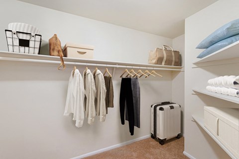 a walk in closet with a rack of clothes and a suitcase