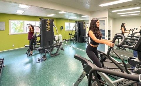 Two women working out on exercise machines in a gym.