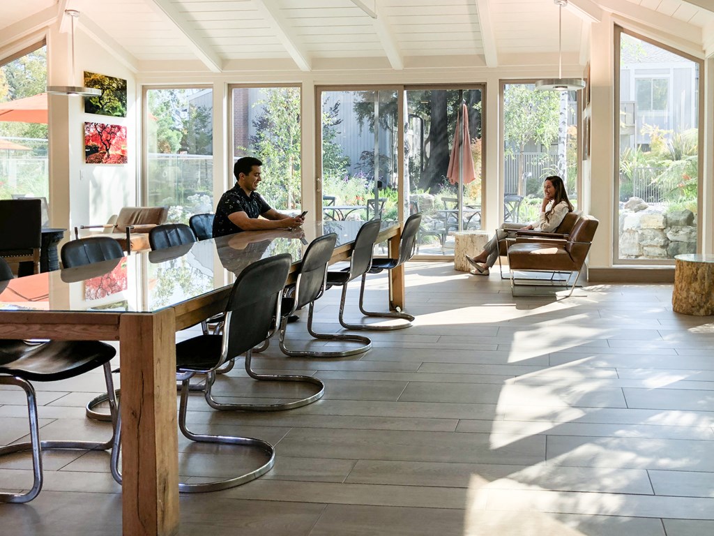 people sitting at a long table in a room with windows