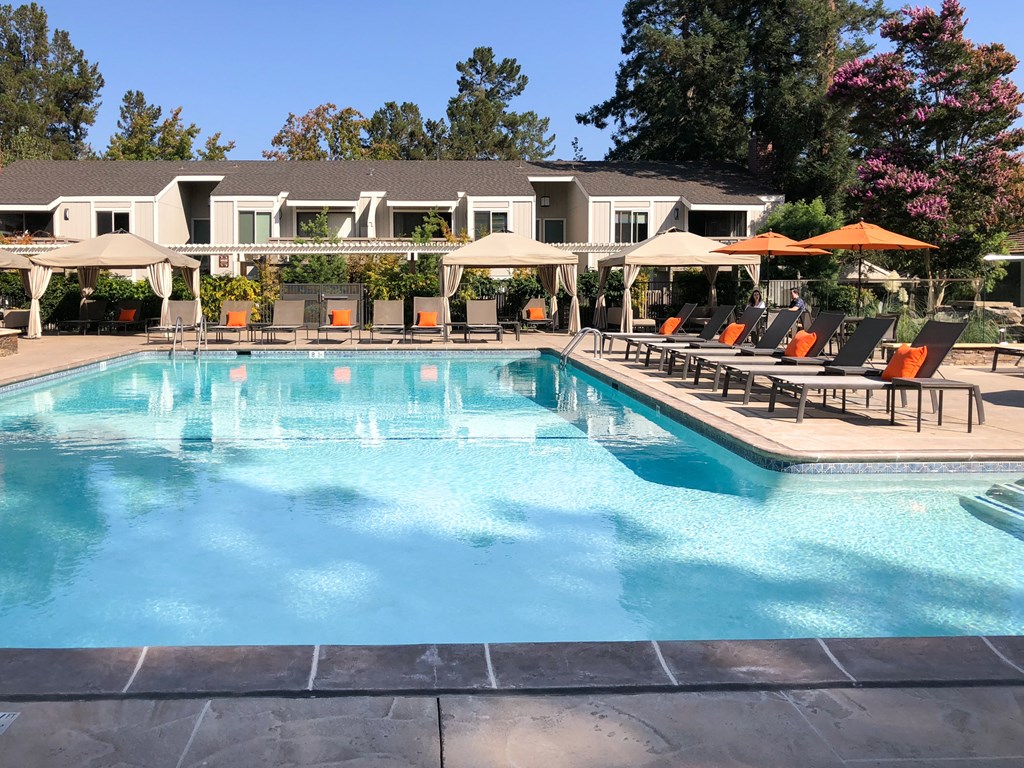 a swimming pool with chairs and umbrellas in front of a resort style pool